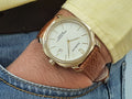 A gold-colored ultra-thin automatic date watch with a brown leather band and a white dial, displayed against a plain background.